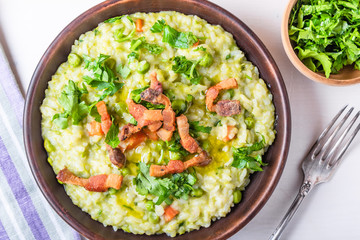 Traditional Italian risotto with peas, carrots and fried bacon, pancetta in rustic style, close-up