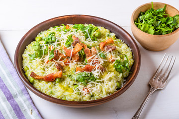 Traditional Italian risotto with peas, carrots and fried bacon, pancetta in rustic style, close-up