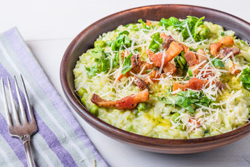 Traditional Italian risotto with peas, carrots and fried bacon, pancetta in rustic style, close-up