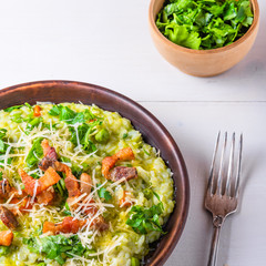 Traditional Italian risotto with peas, carrots and fried bacon, pancetta in rustic style, close-up