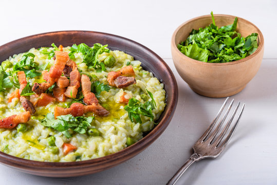 Traditional Italian risotto with peas, carrots and fried bacon, pancetta in rustic style, close-up
