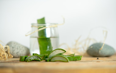 on a wooden table a jar with water and aloe leaf, next to the small fragments cut from the leaves