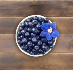 Top view. Bilberres and blue flower. Ripe blueberries with copy space for text. Ripe and tasty blueberries. Blueberries in a white ceramic bowl. Ripe and tasty bilberries 
