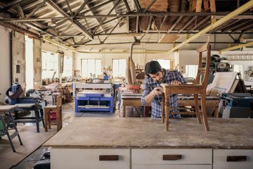 Fototapeta na wymiar Furniture maker sanding a chair on his workshop table