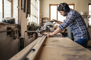 Carpenter cutting wood with a mitre saw in his workshop