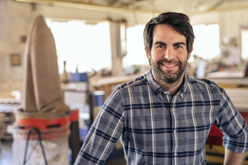 Smiling carpenter standing alone in his large woodworking studio