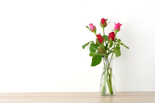 Red and pink roses in glass vase on table and white wall background with copy space, Happy valentine's day concept