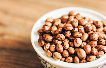 Beans (Phaseolus) in white porcelain bowl on wooden background, vegetarian concept.
