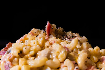 Spaghetti carbonara bacon cheese close up isolated on black background, selective focus