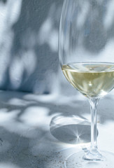 White wine standing in front of a white concrete wall with shadows of leaves on a sunny summer day