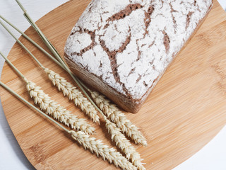 loaf of rye bread on a wooden board, a few ears