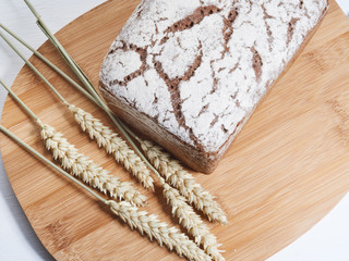 loaf of rye bread on a wooden board, a few ears