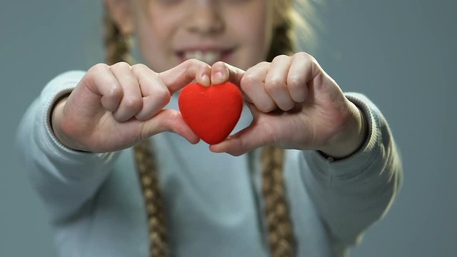 Happy cute girl showing toy heart into camera, feeling herself loved and needed