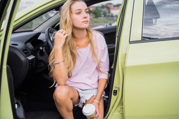 the girl is sitting in the car and drinking coffee