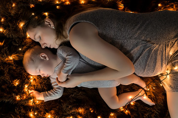 Fototapeta na wymiar A young mother and her baby are sleeping on a fluffy brown blanket, lights are spread around them