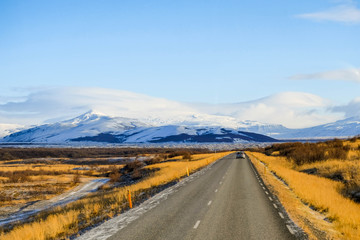 Fototapeta na wymiar Long Road in iceland with Snow mounrtain background and small car drive on the road