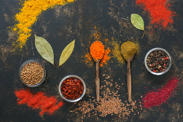A variety of colored spices background. Spices in wooden spoons on a dark rustic background. View from above.
