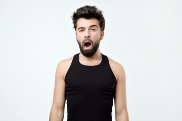 Sleepy young man yawning, waking up isolated on gray background