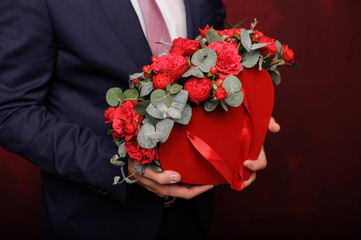 Young man holding in a hand a red box of beautiful roses