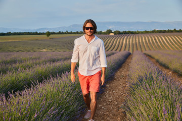 The beautiful brutal young man with long brunette hair poses in the field of lavender.