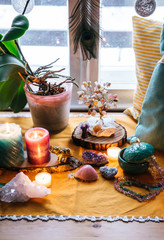 Feng Shui altar at home in living room or bed room. Attracting wealth and prosperity concept. Crystal clusters, wire tree with gemstones, golden Buddah figure on table and window sill. Vibrant colors.
