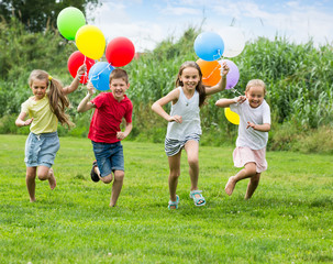children running with air balloons in park .