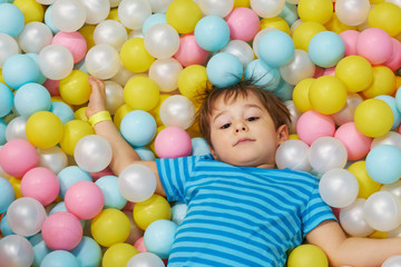 Fototapeta na wymiar child of three years old is playing in a ball pool. boy smiling spends fun time in the nursery.