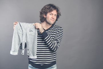 Young caucasian male boasting about new stylish baby clothes for his son holding in hands and demonstrating grey pants to camera. Man smiling looking at camera and bragging new clothes on. Copy space