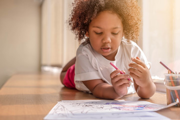 Little toddler girl laying down concentrate on drawing.  Mix African girl learn and play in the pre-school class. Children enjoy hand writing. 3 years girl enjoy playing at nursery.