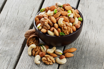 Wooden bowl with mixed nuts on a wooden gray background. Walnut, pistachios, almonds, hazelnuts and cashews, walnut.