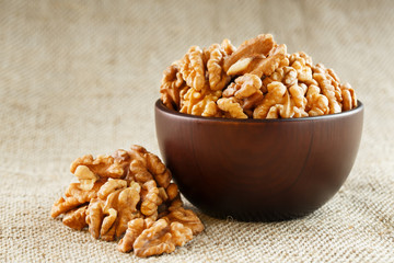 Peeled walnuts in a wooden, dark brown cup on a burlap cloth.