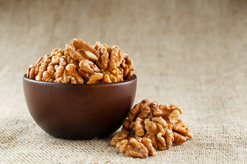 Peeled walnuts in a wooden, dark brown cup on a burlap cloth.