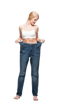 Full Length View Of Surprised Young Woman In Oversized Jeans Looking Down Isolated On White