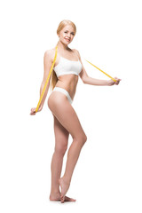 full length view of beautiful young woman in underwear holding measuring tape and smiling at camera isolated on white