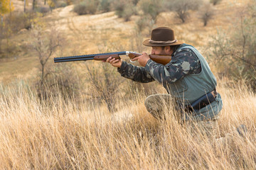 Fototapeta premium Hunter with a hat and a gun in search of prey in the steppe 