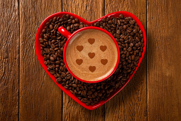 Red cup and coffee saucer in heart shape with decorated coffee on old wood background. Top View. Heart shape in coffee.