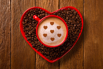 Red cup and coffee saucer in heart shape with decorated coffee on old wood background. Top View. Heart shape in coffee.