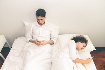 Young couple looking smartphone on the bed.Both of couple don't care each other after quarrel