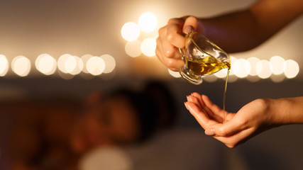 Masseur pouring massage oil, woman lying on background