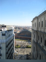 Fototapeta premium 2ª vista urbana desde altura con primer plano de edificios históricos y detrás con calzada, coches, antigua estación de tren y horizonte de fondo ciudad con nuves y cielo azul