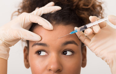 African-american woman getting botox injection in forehead - obrazy, fototapety, plakaty