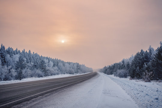 Fog on a winter automobile highway on either side of the forest in hoarfrost. Siberian Winter Tale.