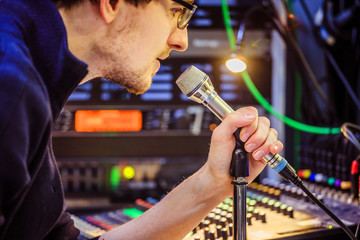Studio recording: Young man wspeaks into a microphone, studio in the blurry background