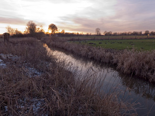 Abendstimmung an einem Bach im Norden von Deutschland. An Ufer liegt etwas Schnee und das trockene...