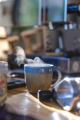 close up a ceramic cup of hot smoke coffee on wooden table with blurred coffee machine in background