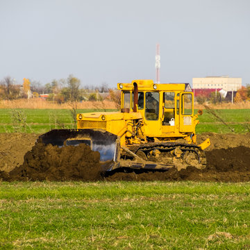 The yellow tractor with attached grederom makes ground leveling.