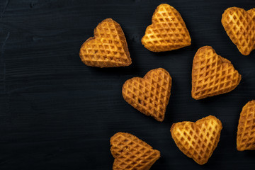 Heart-shaped cookies with jam and candy, over the head on black wood.