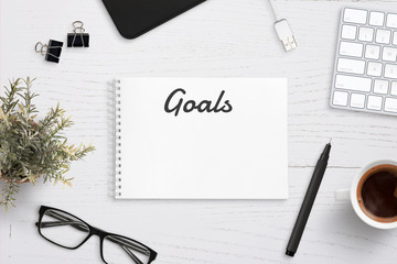 Creating goals list on notepad on office desk surrounded with office supplies. White wooden work...