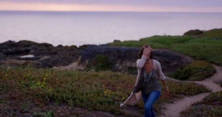 Young happy woman walks towards camera with beautiful walking trail and ocean in background - Powered by Adobe