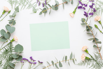 Flowers composition. Paper blank, carnation flowers, eucalyptus branches on pastel  background. Flat lay, top view, copy spaceFlat lay stiil life.